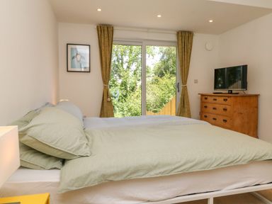 A bedroom with a bed a wooden dresser and a television near a sliding glass door with curtains at Valise in Bideford
