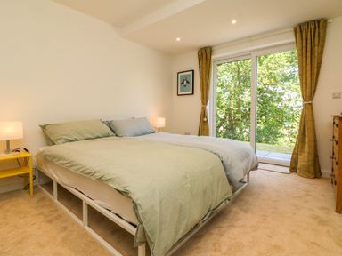 A bedroom with a double bed yellow side table two lamps wooden dresser and sliding glass door with curtains at Valise in Bideford