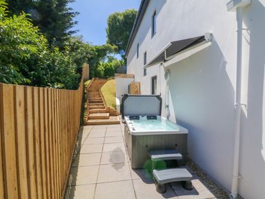 An outdoor patio area with a hot tub and steps next to a white house with wooden fencing at Valise in Bideford
