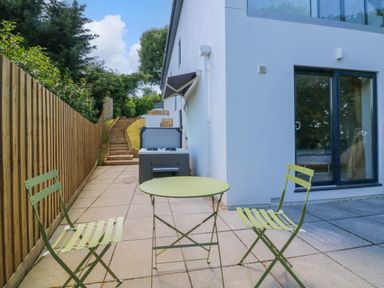 A patio with a green metal table and two chairs beside a white building with sliding glass doors at Valise in Bideford