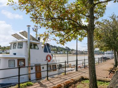A boat moored along a riverside walkway with trees and benches at Valise in Bideford