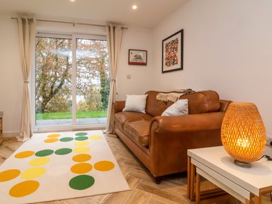 A living room with a brown leather sofa two white pillows a patterned rug and a wicker lamp on a table at Valise in Bideford