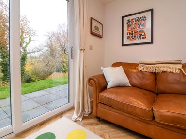 A corner of a room with a brown leather sofa a pillow two framed pictures on the wall and a glass door leading to a garden at Valise in Bideford