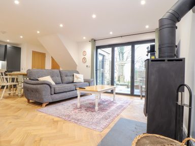 A living room with a grey sofa white coffee table wood burning stove and glass doors leading outside at Wildwood in Newquay