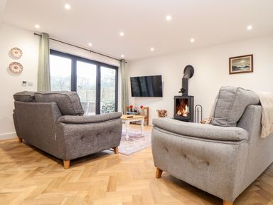 A living room with two grey sofas a wood burning stove and a wall mounted TV at Wildwood in Newquay
