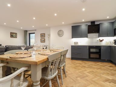 A dining table with place settings and chairs in a kitchen and living area at Wildwood in Newquay