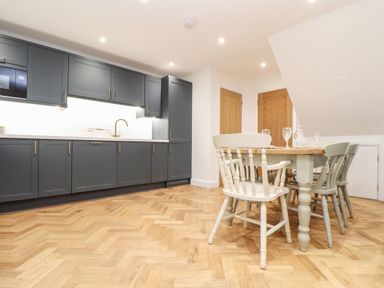 A kitchen with dark cabinets and a wooden dining table with chairs at Wildwood in Newquay