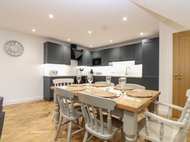 A kitchen with dark cabinets dining table with six chairs and place settings at Wildwood in Newquay