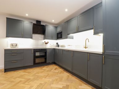 A kitchen with grey cabinets wooden floor and white countertops at Wildwood in Newquay