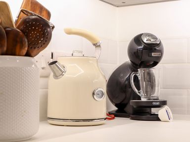 A kitchen counter with a white kettle a black coffee machine a glass cup and wooden utensils in a white container at Wildwood in Newquay