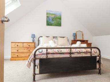 A bedroom with a metal bed frame two wooden dressers and a skylight window at Wildwood in Newquay