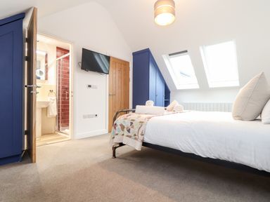 A bedroom with a double bed with white linens and towels on top two skylight windows blue built-in wardrobes a wall-mounted television and a door leading to a bathroom at Wildwood in Newquay