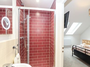 A bathroom with a shower with red tiles and a bedroom with skylights and a bed with towels at Wildwood in Newquay