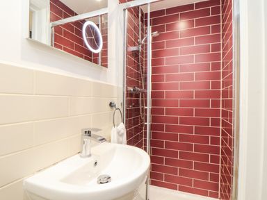 A bathroom with a white sink and faucet a round towel ring with towel a shower with glass door and red tiled walls Wildwood Newquay