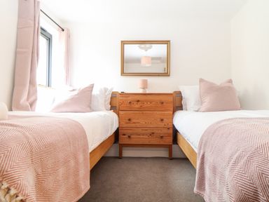 A bedroom with two single beds with pink and white bedding and a wooden chest of drawers with a mirror above at Wildwood in Newquay