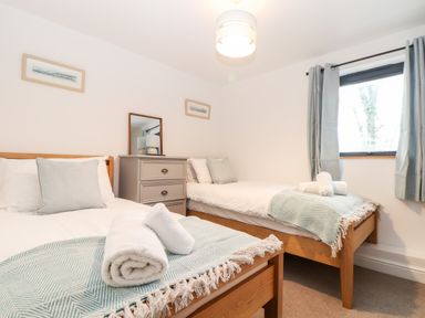 A bedroom with two single beds side by side a dresser with a mirror and a window with curtains at Wildwood in Newquay