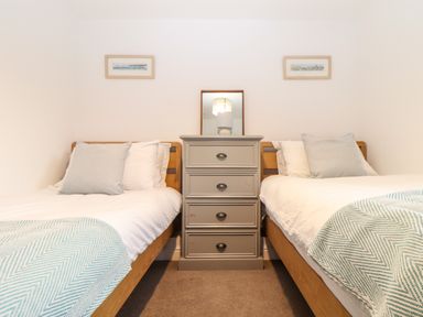 A bedroom with two single beds separated by a gray chest of drawers with a lamp and mirror at Wildwood in Newquay