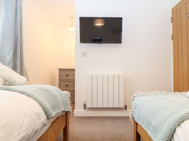 A bedroom with two beds covered with blue blankets a wall-mounted TV and a wooden door at Wildwood in Newquay