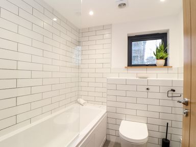 A bathroom with a bathtub, toilet, small window with a plant on the sill at Wildwood in Newquay