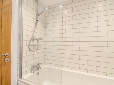 A bathroom with a bathtub shower combination and white tiled walls at Wildwood in Newquay