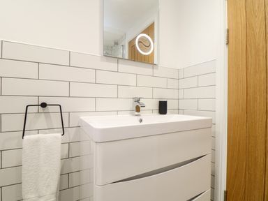 A bathroom sink with white tiles on the wall a towel on a black holder and a mirror above at Wildwood in Newquay