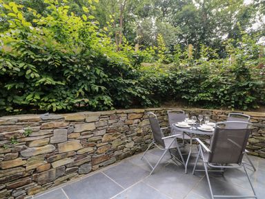 An outdoor patio area with a round dining table set for four and a stone wall with greenery behind at Wildwood in Newquay