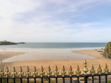 A sandy beach with ocean waves and a decorative metal fence in the foreground at Wildwood in Newquay