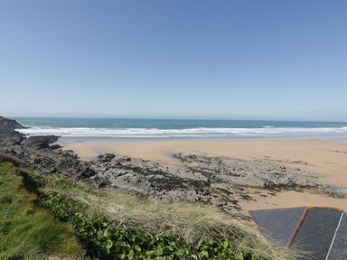 A sandy beach with rocky outcrops and ocean waves under a clear sky at Wildwood in Newquay