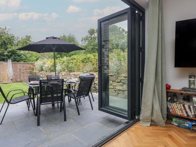 A patio with outdoor dining table and chairs with umbrella in a garden as seen from inside a room at Wildwood in Newquay