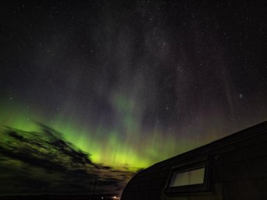 A night sky with stars and northern lights above a building roof at Heisgeir in Sollas Isle Of North Uist