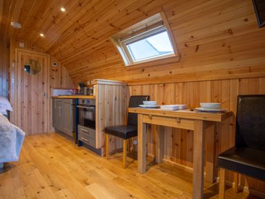 A wooden kitchenette with a stove sink and small dining table with two chairs under a skylight at Heisgeir in Sollas Isle Of North Uist
