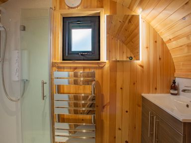 A bathroom with a shower, small window, towel radiator, illuminated mirror, sink, and wooden walls at Heisgeir in Sollas Isle Of North Uist