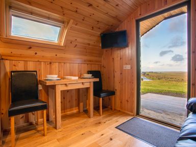 A wooden dining area with a table and two chairs next to an open door showing a grassy landscape at Heisgeir Sollas Isle Of North Uist