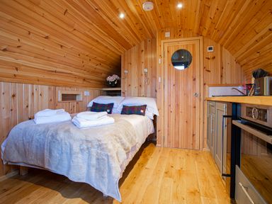 A wooden interior room with a bed towels pillows kitchen cabinets and an oven at Heisgeir in Sollas Isle Of North Uist