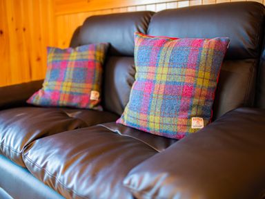 A brown leather sofa with two colorful plaid cushions in a wooden room at Heisgeir in Sollas Isle Of North Uist