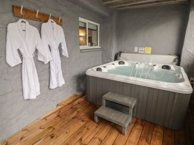 An indoor hot tub with water jets and a small step stool next to two white bathrobes hanging on hooks on a gray stone wall at Le Durkestrete Cellar in Haverfordwest