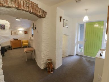 An entryway with a green door and white walls next to a living area with chairs and framed pictures at Le Durkestrete Cellar in Haverfordwest