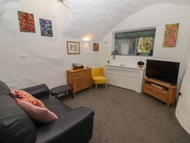 A living room with a black sofa yellow chair wooden cabinets and a TV at Le Durkestrete Cellar in Haverfordwest