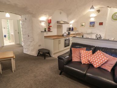 A living room with a black leather sofa with cushions next to a kitchen area with white cabinets at Le Durkestrete Cellar in Haverfordwest