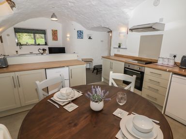 A kitchen and dining area with wooden table set for two and white cabinets at Le Durkestrete Cellar in Haverfordwest