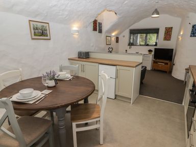 A kitchen and dining area with a round wooden table and four chairs in a white vaulted room at Le Durkestrete Cellar in Haverfordwest