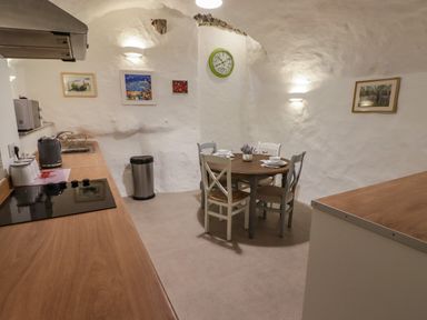 A kitchen with a round dining table set for four and kitchen appliances on wooden countertops at Le Durkestrete Cellar in Haverfordwest