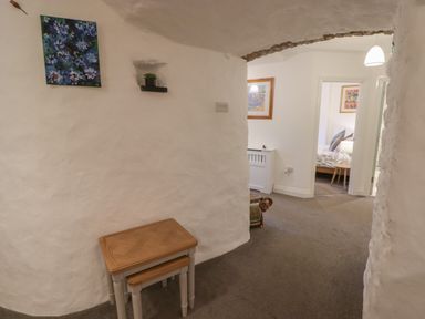 A hallway with white curved walls a set of nested wooden tables a small plant on a wall shelf and a floral painting at Le Durkestrete Cellar in Haverfordwest
