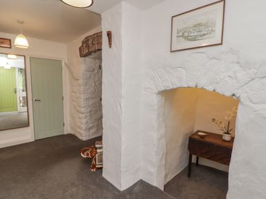 A hallway with white textured walls a green door a mirror and a wooden table with a vase and flowers in an alcove at Le Durkestrete Cellar in Haverfordwest