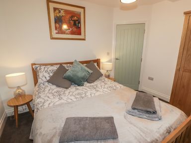 A bedroom with a double bed a wooden wardrobe bedside tables lamps and a painting on the wall at Le Durkestrete Cellar in Haverfordwest