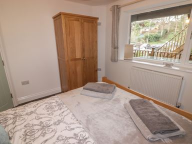 A bedroom with a bed, wooden wardrobe, radiator under a window, and folded towels on the bed at Le Durkestrete Cellar in Haverfordwest