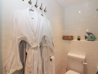 A bathroom with white bathrobes hanging on hooks a toilet with a basket plant and fish decoration on a tiled ledge at Le Durkestrete Cellar in Haverfordwest