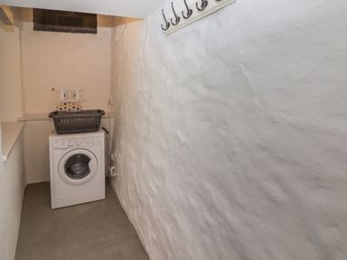 A narrow laundry room with a washing machine and a laundry basket on top at Le Durkestrete Cellar in Haverfordwest