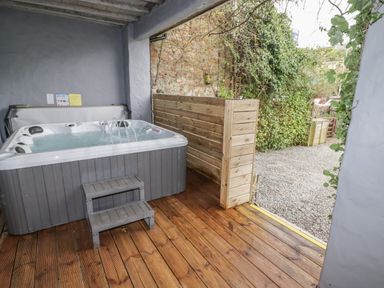 An outdoor covered area with a hot tub and wooden steps leading to a gravel garden at Le Durkestrete Cellar in Haverfordwest