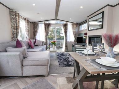 A living room with a grey sectional sofa purple cushions coffee table dining table set with dishes and glassware at Ginger Fox Lodge in East Heslerton near Cayton